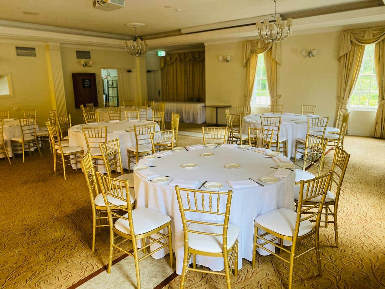 A spacious room with white tables and chairs available for Gold Tiffany Chair Hire.