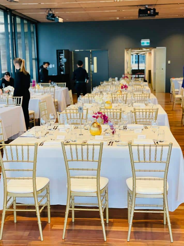 A spacious room with tables and Gold Tiffany chairs set up.