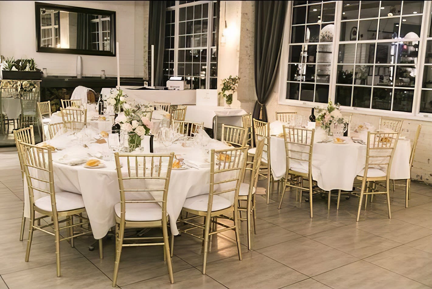 A room with tables and chairs set up for a wedding reception, featuring elegant Gold Tiffany Chair Hire.