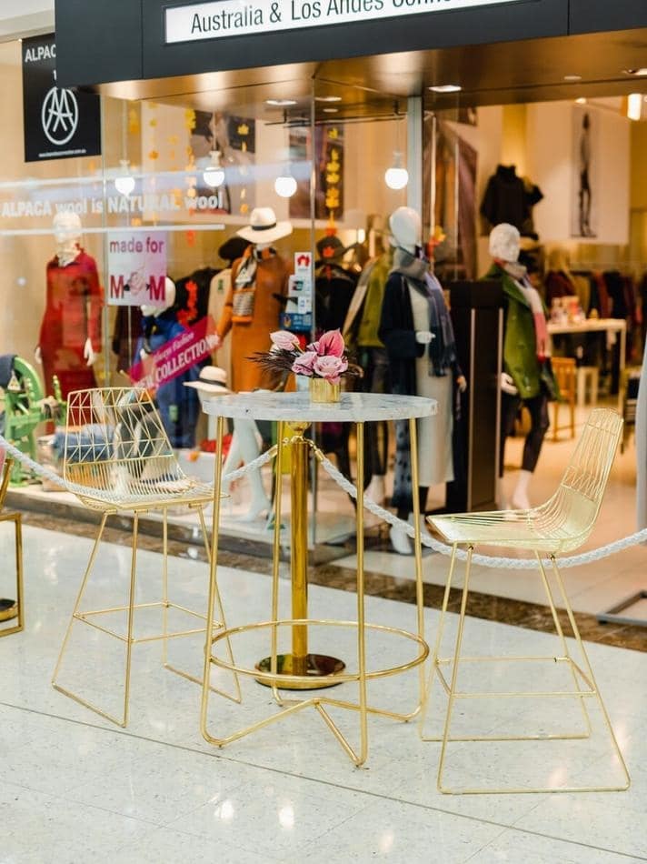 A gold table and chairs in a shopping mall available for Gold Wire Stool / Arrow Stool Hire.