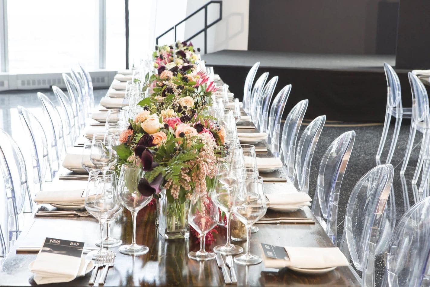 A long table set with clear Victorian ghost chairs and adorned with beautiful flowers.