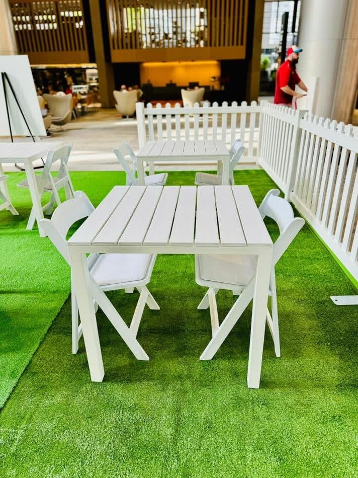 A white table and chairs on a green grass park setting. White padded folding chairs (Gladiator chair) available for hire.
