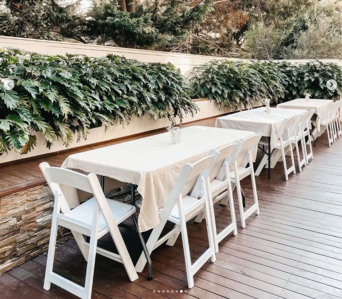 A white table and chairs set up on a wooden deck, including White Padded Folding Chairs (Gladiator chairs).