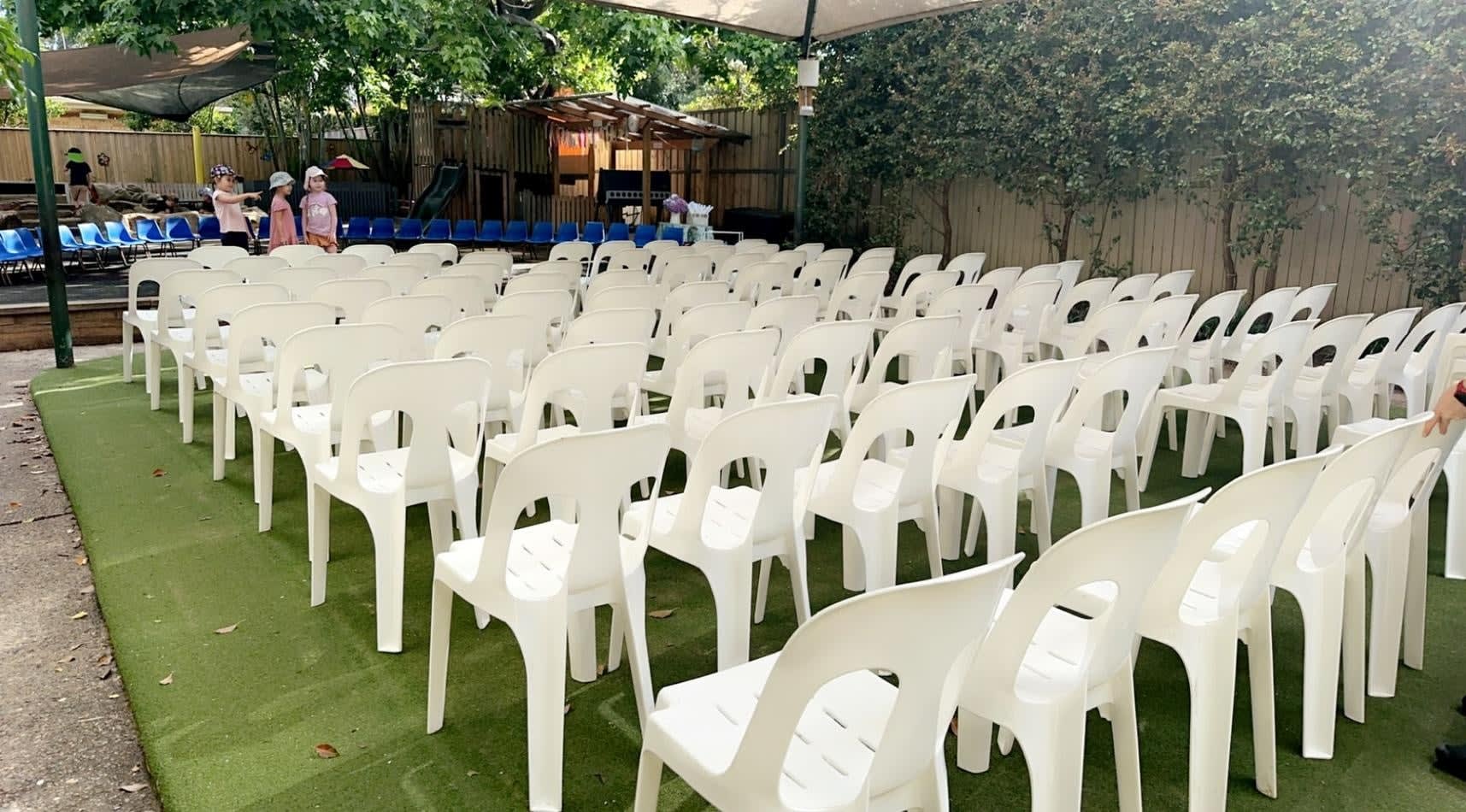 A large group of white plastic stackable chairs set up in an outdoor area.