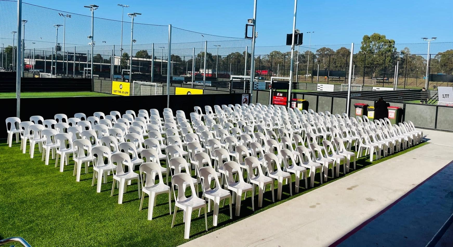 A large group of white plastic chairs on a grass field.