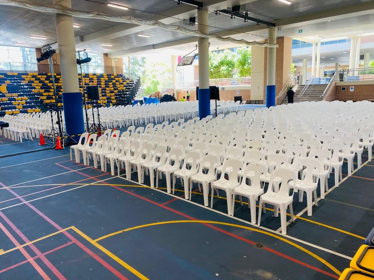 A gymnasium filled with white plastic stackable chairs and a basketball court.