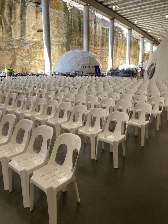 A large room full of white plastic stackable chairs in front of a rock wall.