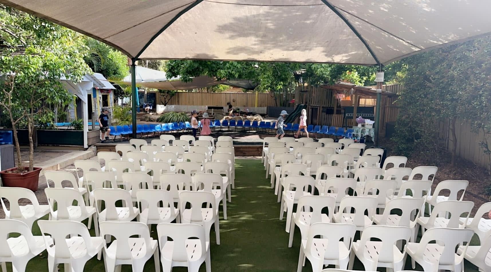 An outdoor ceremony set up with white plastic stackable chairs and a canopy.