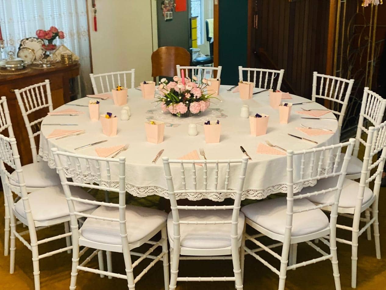 A round table with white Tiffany chairs and pink tablecloths.