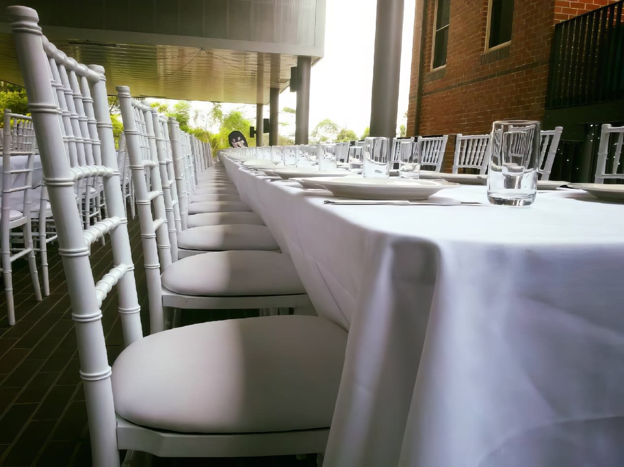 A table set up with white Tiffany chairs and white tablecloths.