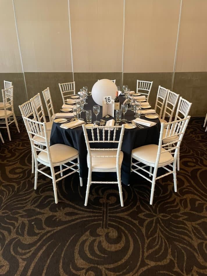 A white table and chairs set up in a room, available for White Tiffany Chair Hire.