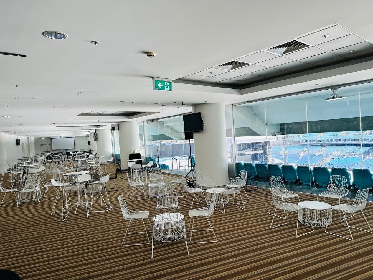 A large room with white wire chairs and tables arranged in the middle of a stadium.