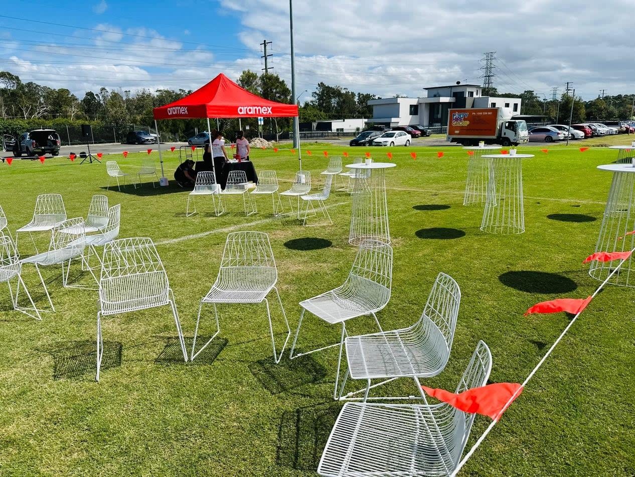 A group of white chairs, specifically the White Wire Chairs, set up on a grassy field.