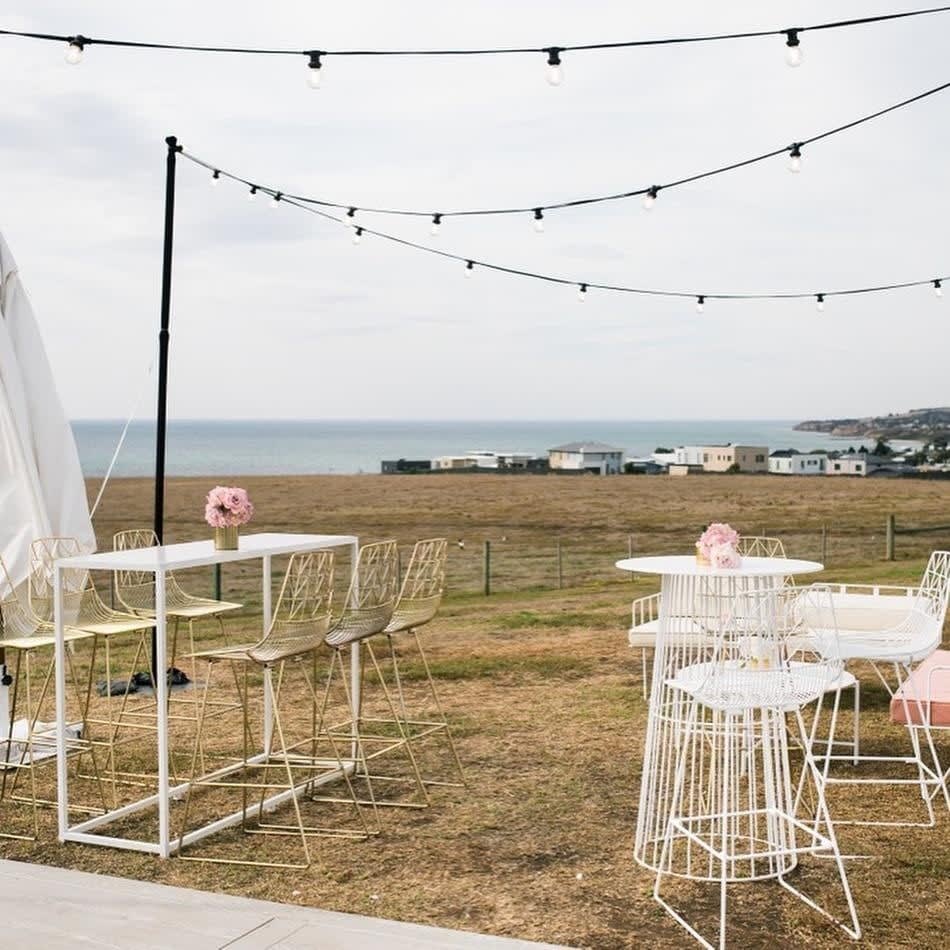 A white table and chairs on a grassy area with a view of the ocean, featuring white chairs.