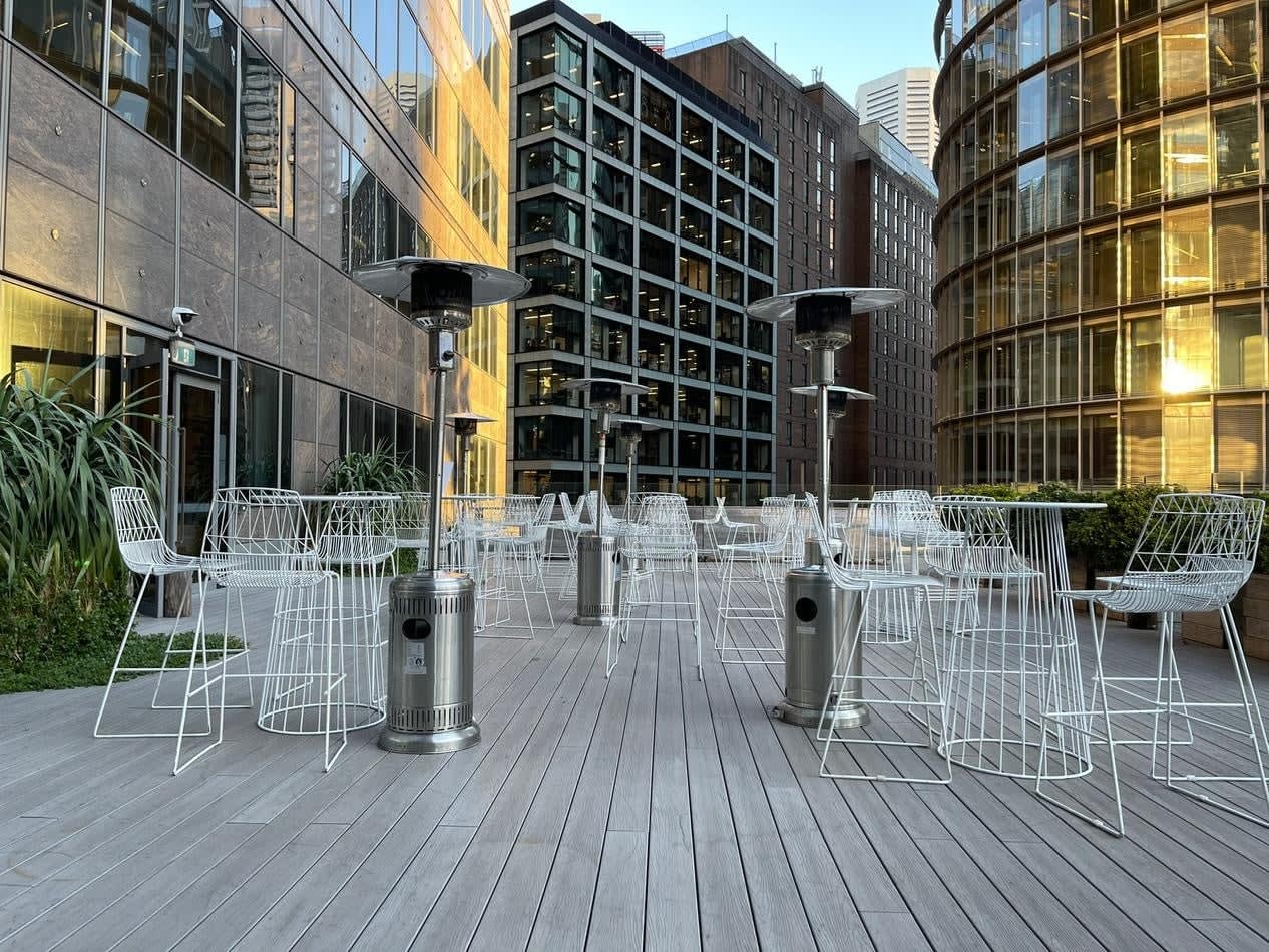 A white patio with chairs and tables in the middle of a city, featuring White Wire Stool seating options.