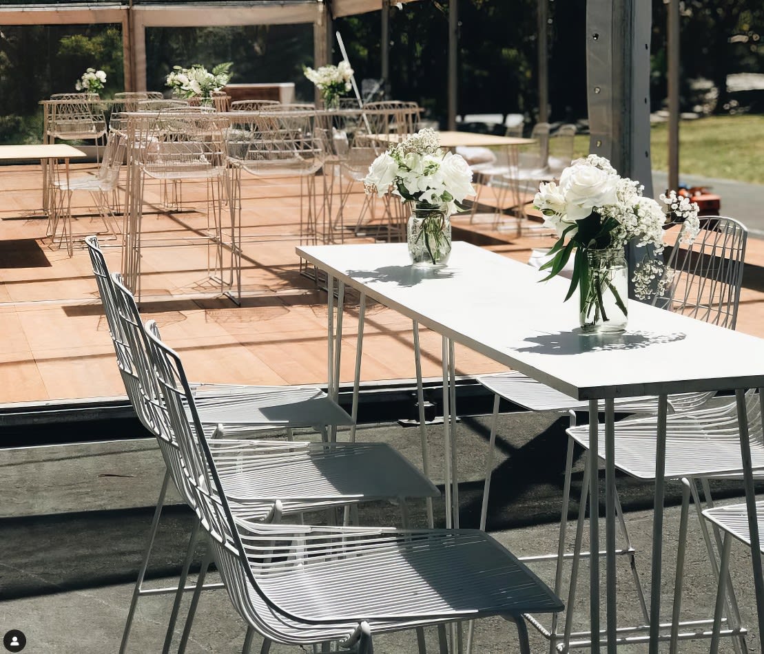 A table set up with white chairs and flowers, featuring a White Wire Stool Hire.