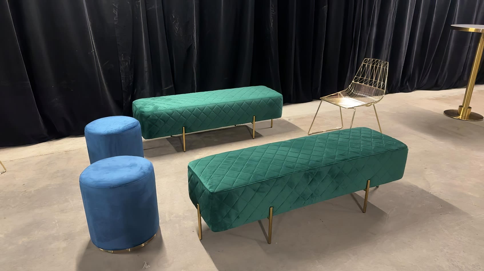 An emerald green velvet bench and two blue stools in a room.