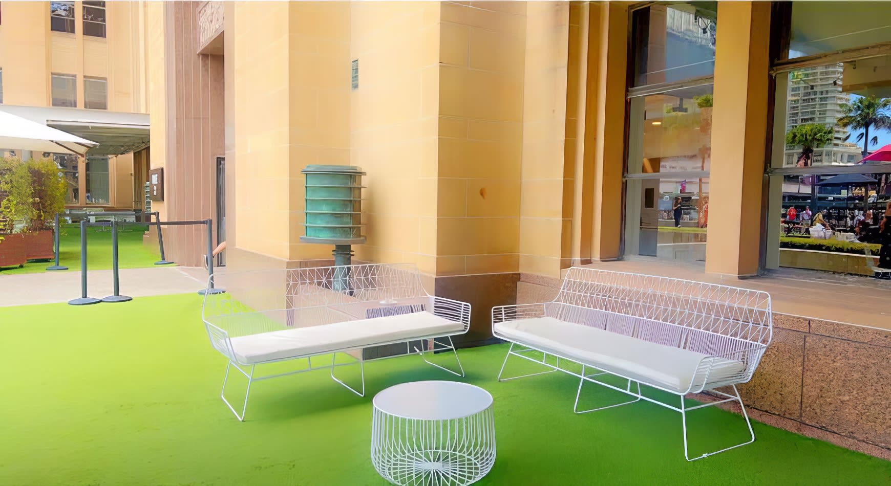 A white table and chairs on a green carpet in front of a building available for White Arrow 3 Seater Lounge Hire.