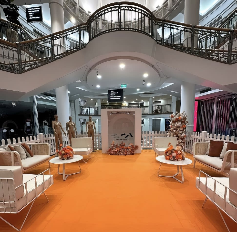 An orange carpet and white furniture, including wire arm chairs hired with white velvet cushions, create a vibrant and inviting ambiance in a mall.