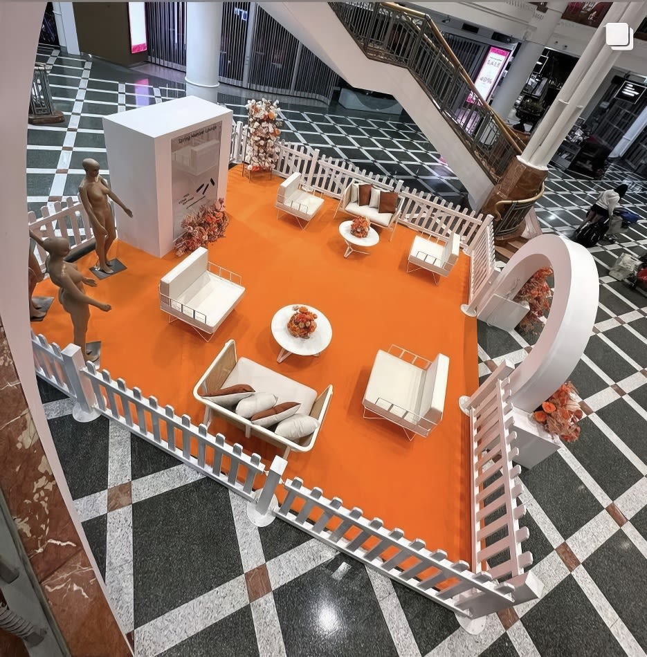 An orange and white display featuring wire arm chair hire with white velvet cushions in a mall.