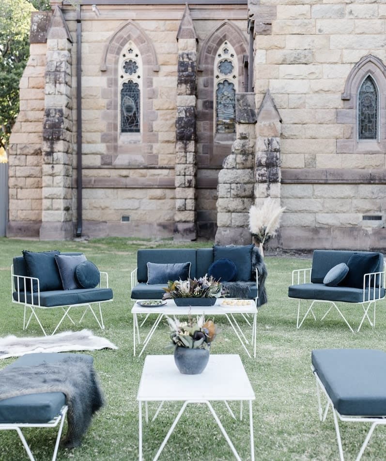 A set of wire sofa lounge with navy blue velvet cushions placed in front of a church.