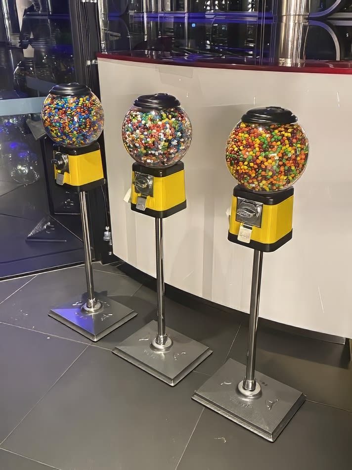 Three gumball machines stand in front of a wall.