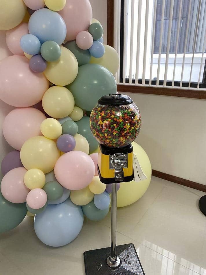         Candy Dispenser Machine Hire - Pkg 1: A gumball machine with balloons in front of it.