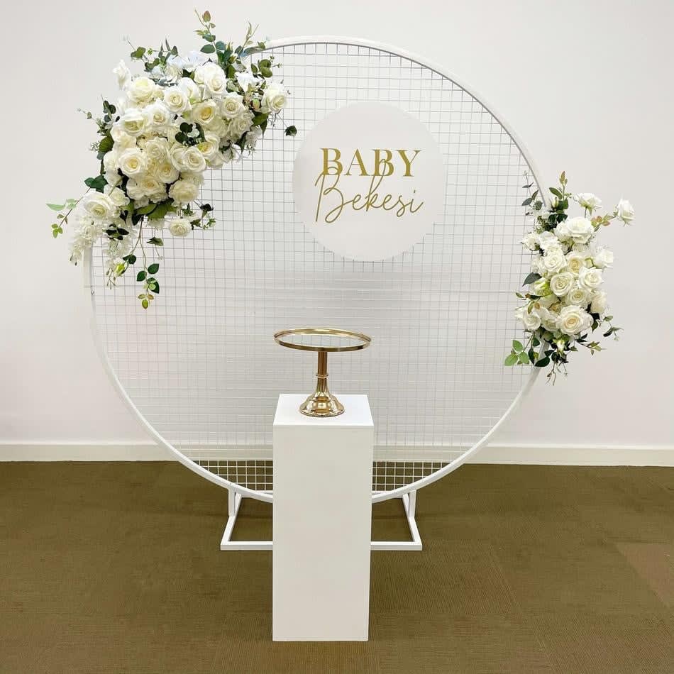 A baby shower stage with a circular white mesh backdrop adorned with white flowers and a golden sign.