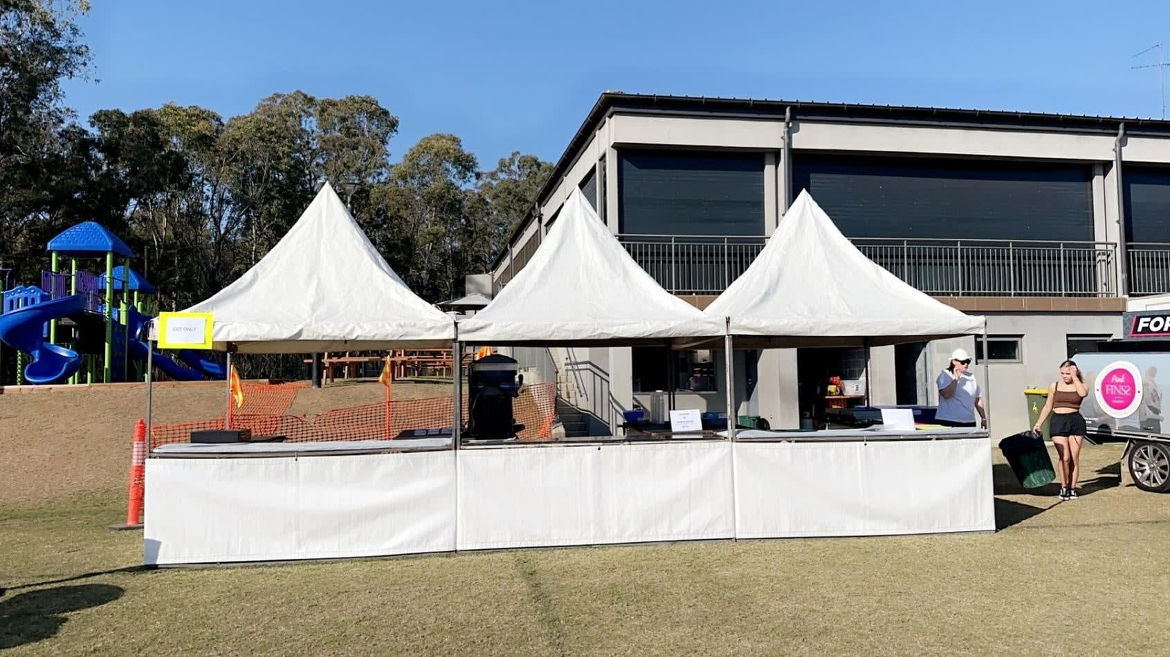 A group of people standing in front of a white tent available for Fete Stall/Tent Hire.