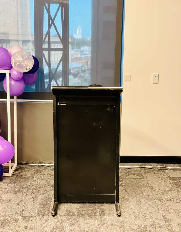 A podium with purple balloons in front of a window available for Lectern Hire.