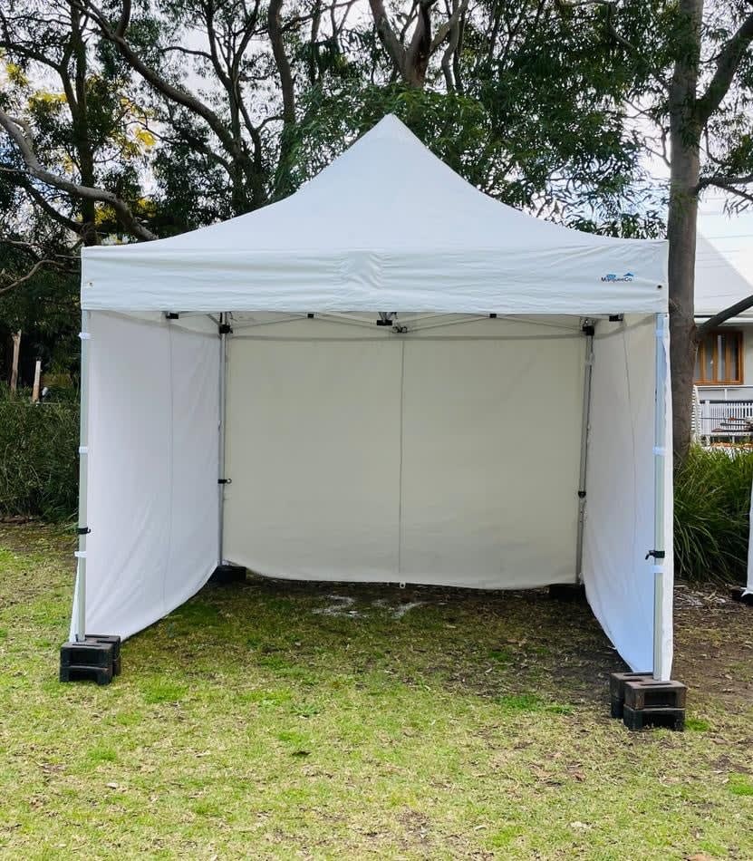 A white 3mx3m pop up tent is set up in a grassy area.