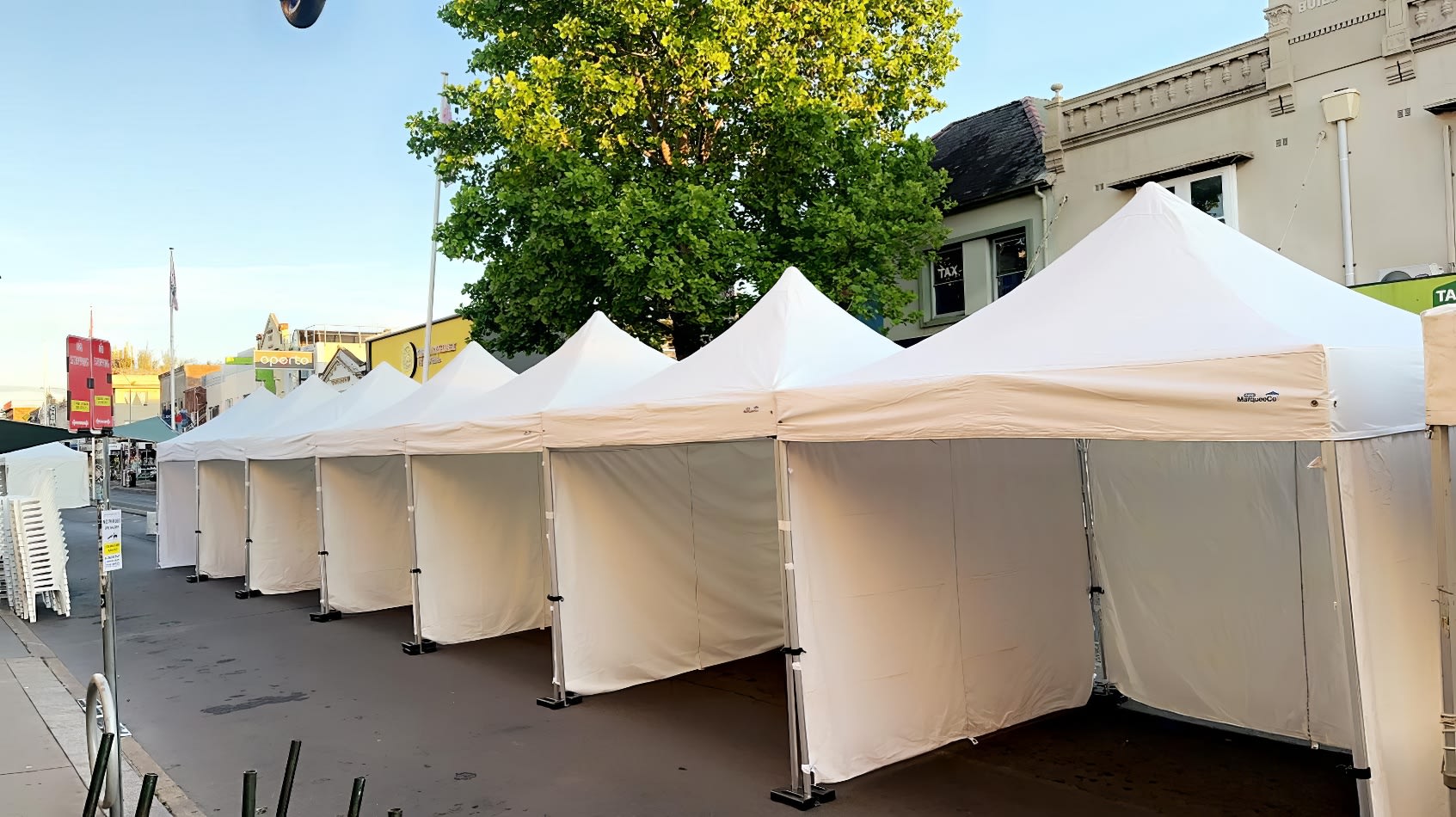 A row of 3mx3m pop up marquees with walls on 3 sides, lined up on a street.