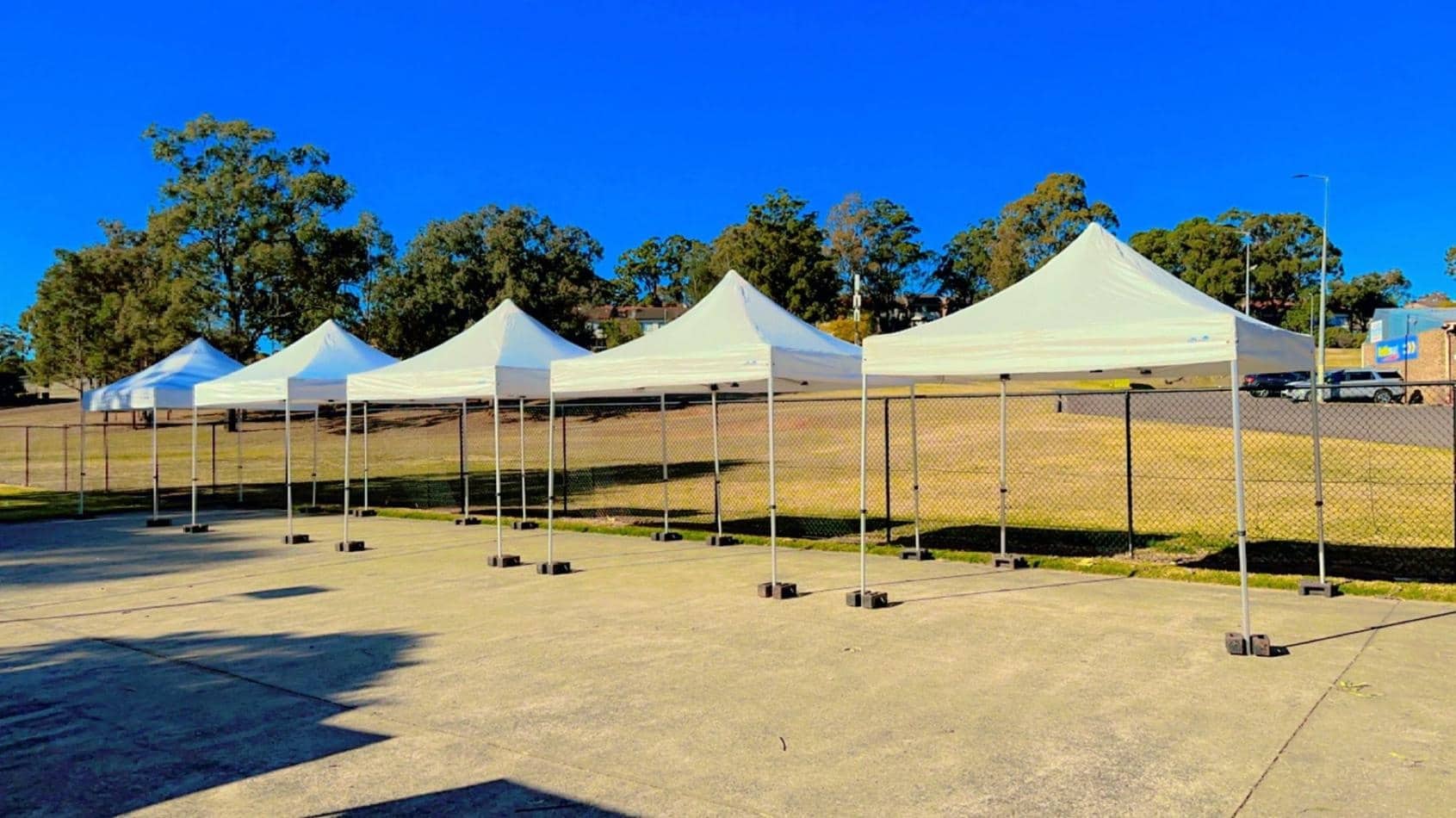 A row of 3mx3m pop-up marquees with white roofs in a parking lot.