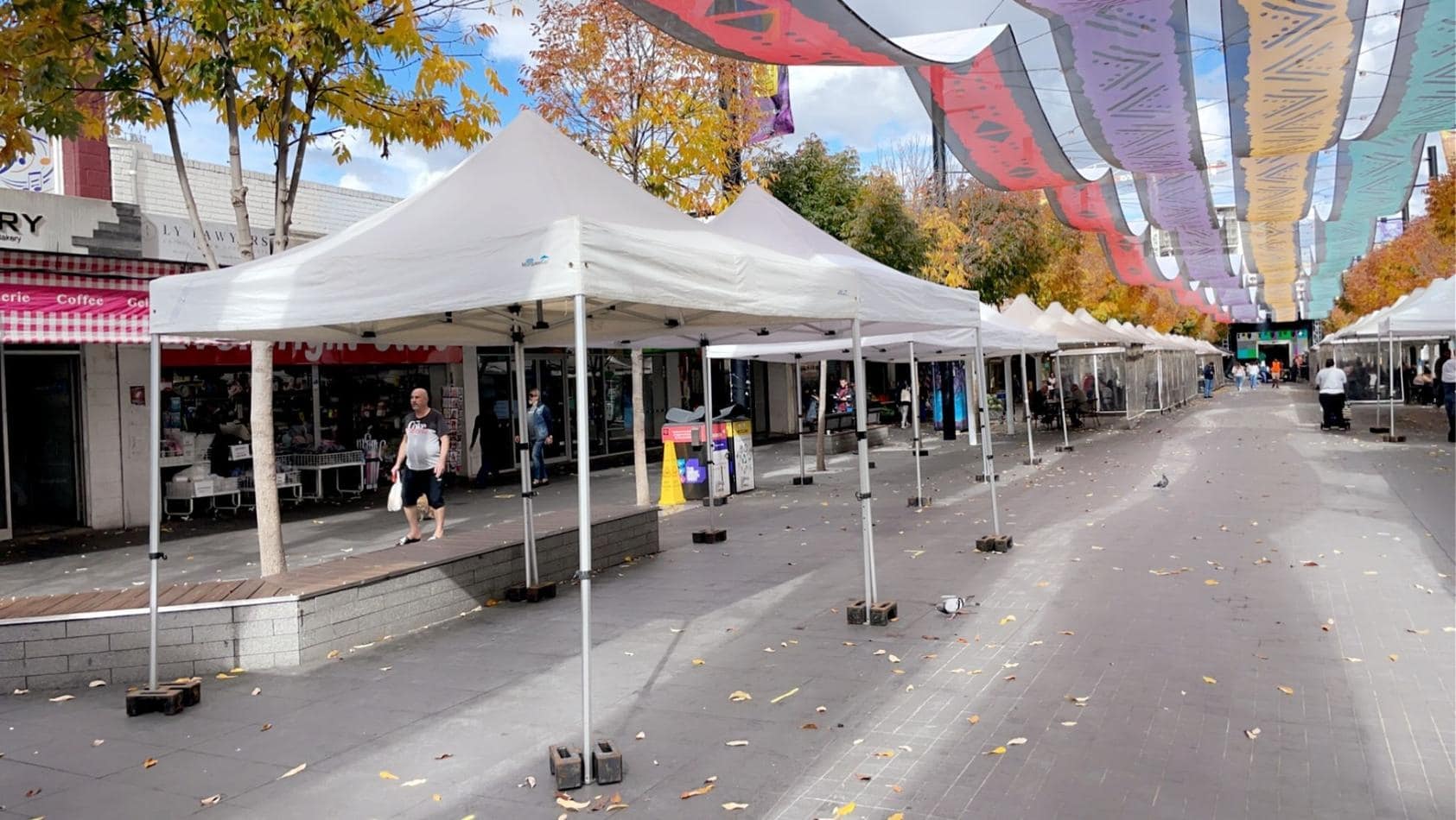 A street lined with 3mx3m pop up marquees, each adorned with a white roof and accompanied by umbrellas.