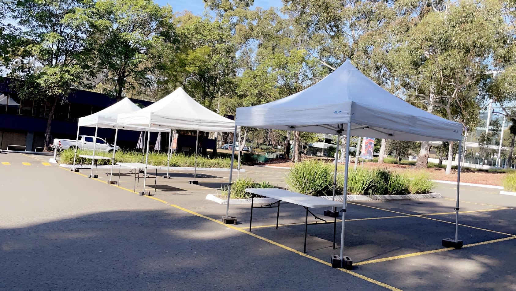 A group of 3mx3m pop-up marquees with white roofs set up in a parking lot.