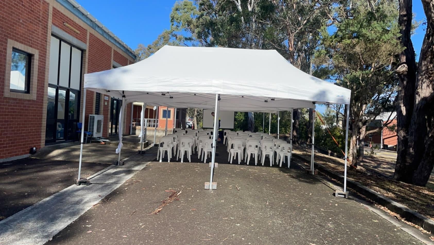 A white 3mx6m pop-up marquee with chairs set up in front of a building.