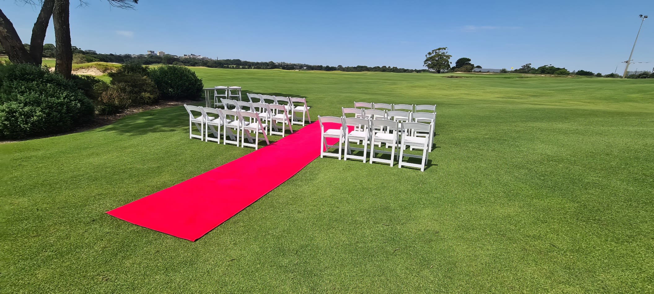 A wedding ceremony set up on a golf course, featuring a luxurious red carpet hire spanning 7m for an elegant entrance.