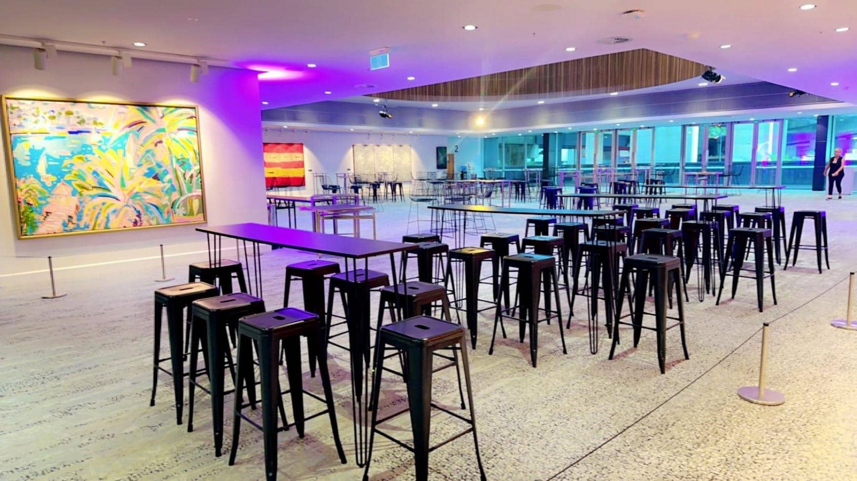 A room with a black hairpin high bar table and stools, adorned with a painting on the wall.