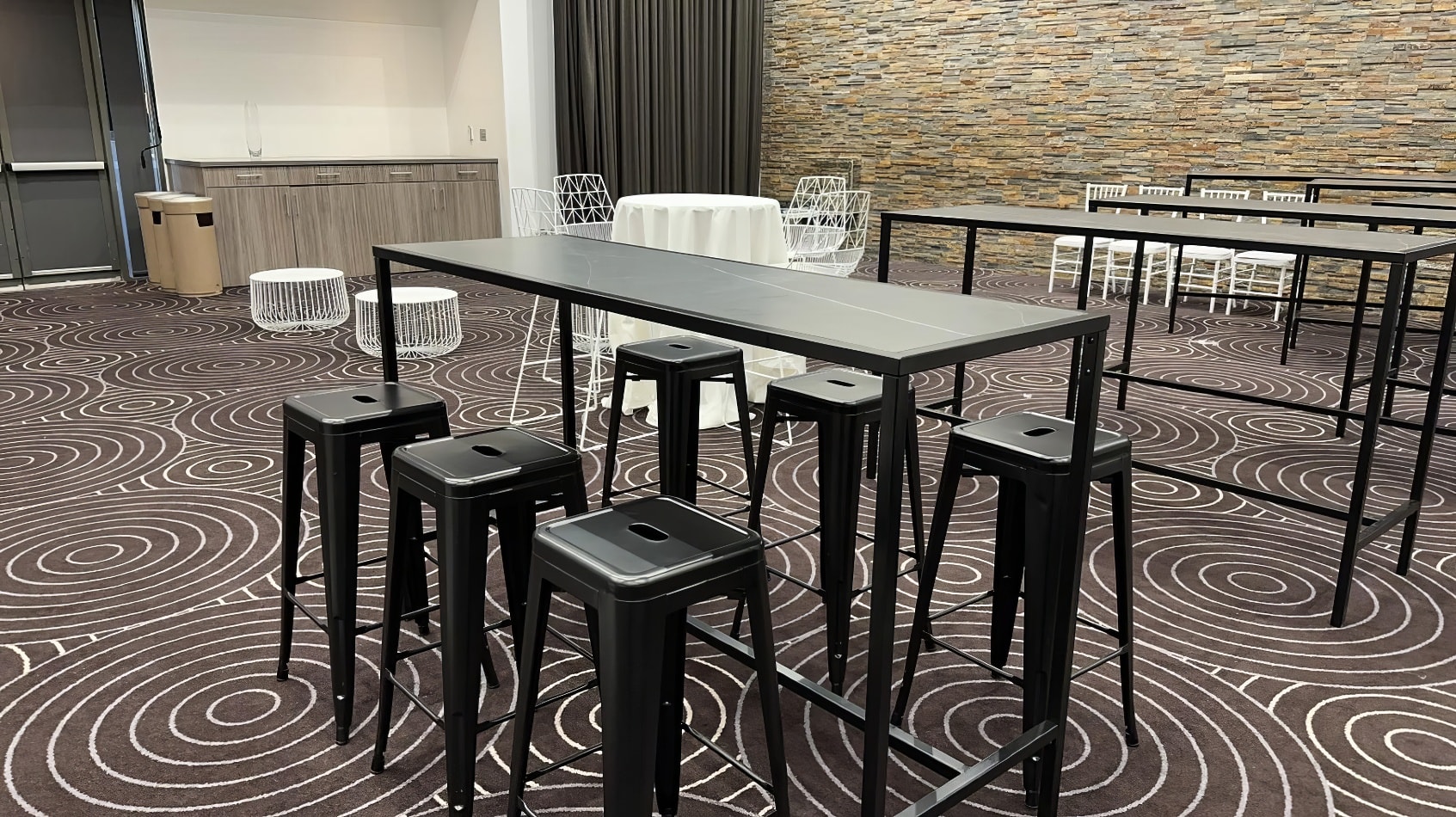 A room with a black rectangular table and stools in it.