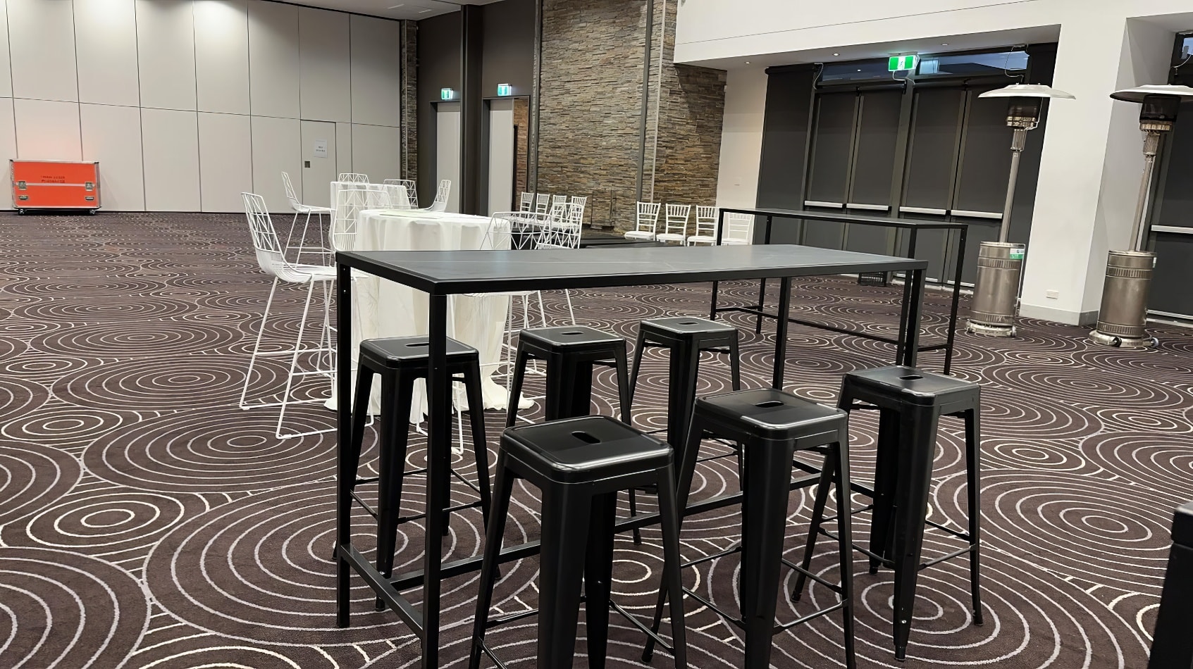 A room with black rectangular tables and stools in it.