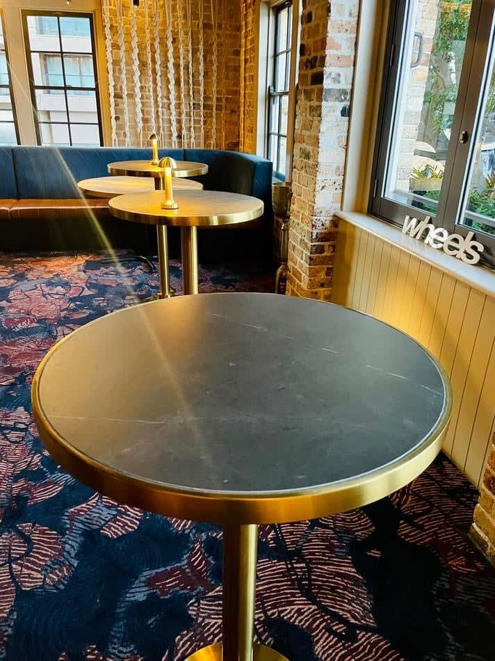 A gold-based round table with a brass cocktail bar design and a black marble top in a room.