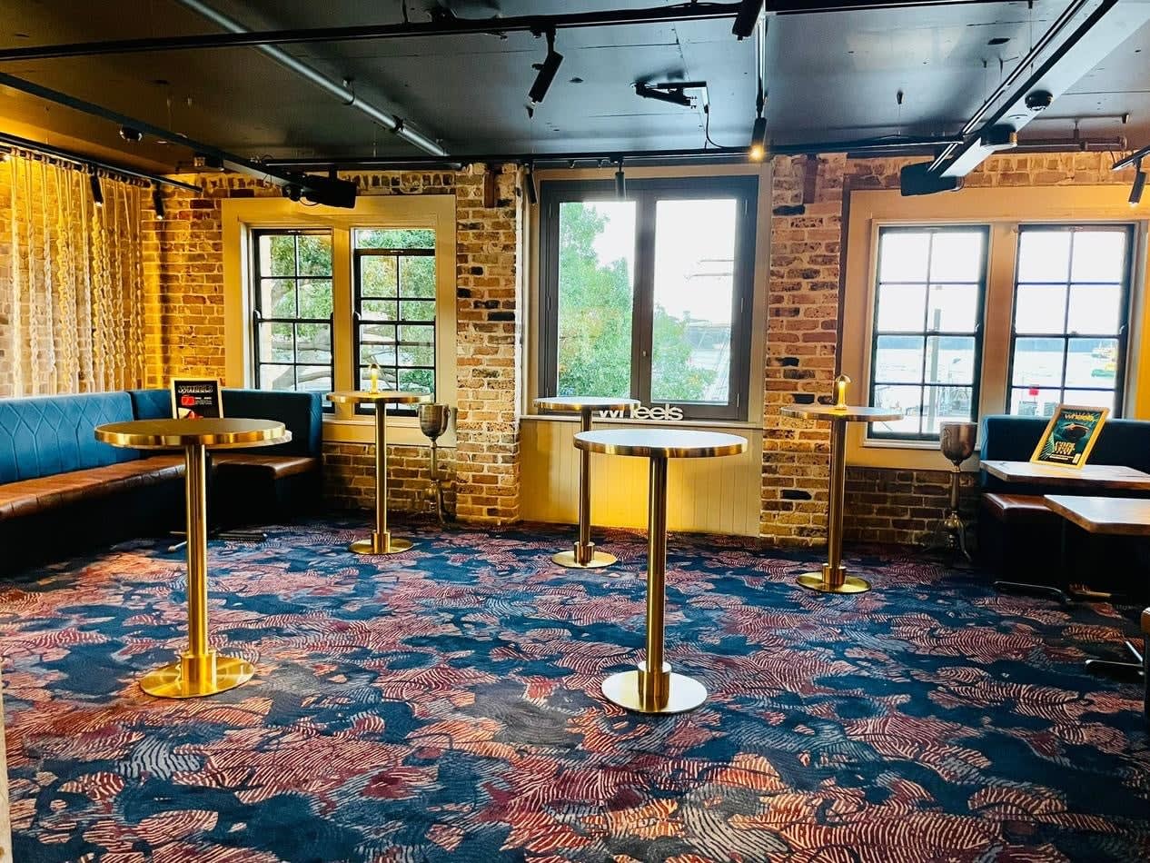 A room with tables and chairs in a brick building, featuring Brass Cocktail Bar Tables with Black Marble Tops.