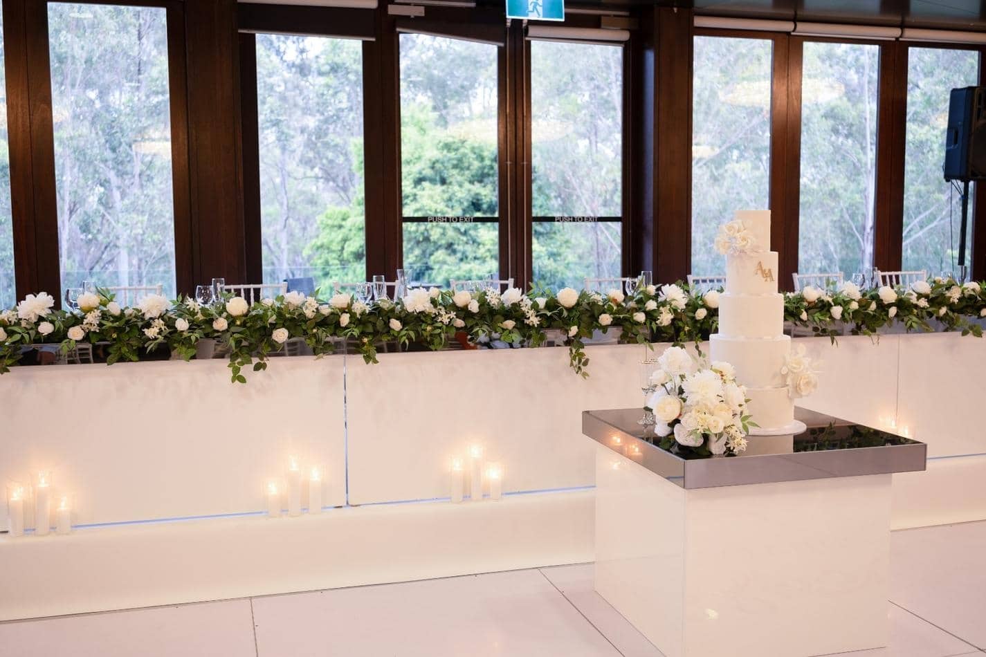 A wedding reception with white flowers and candles on a Gloss Cake Table.
