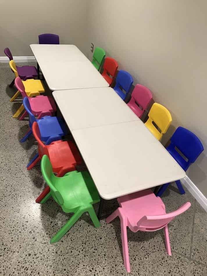 A room full of colorful plastic chairs and tables available for Kids Table Hire.