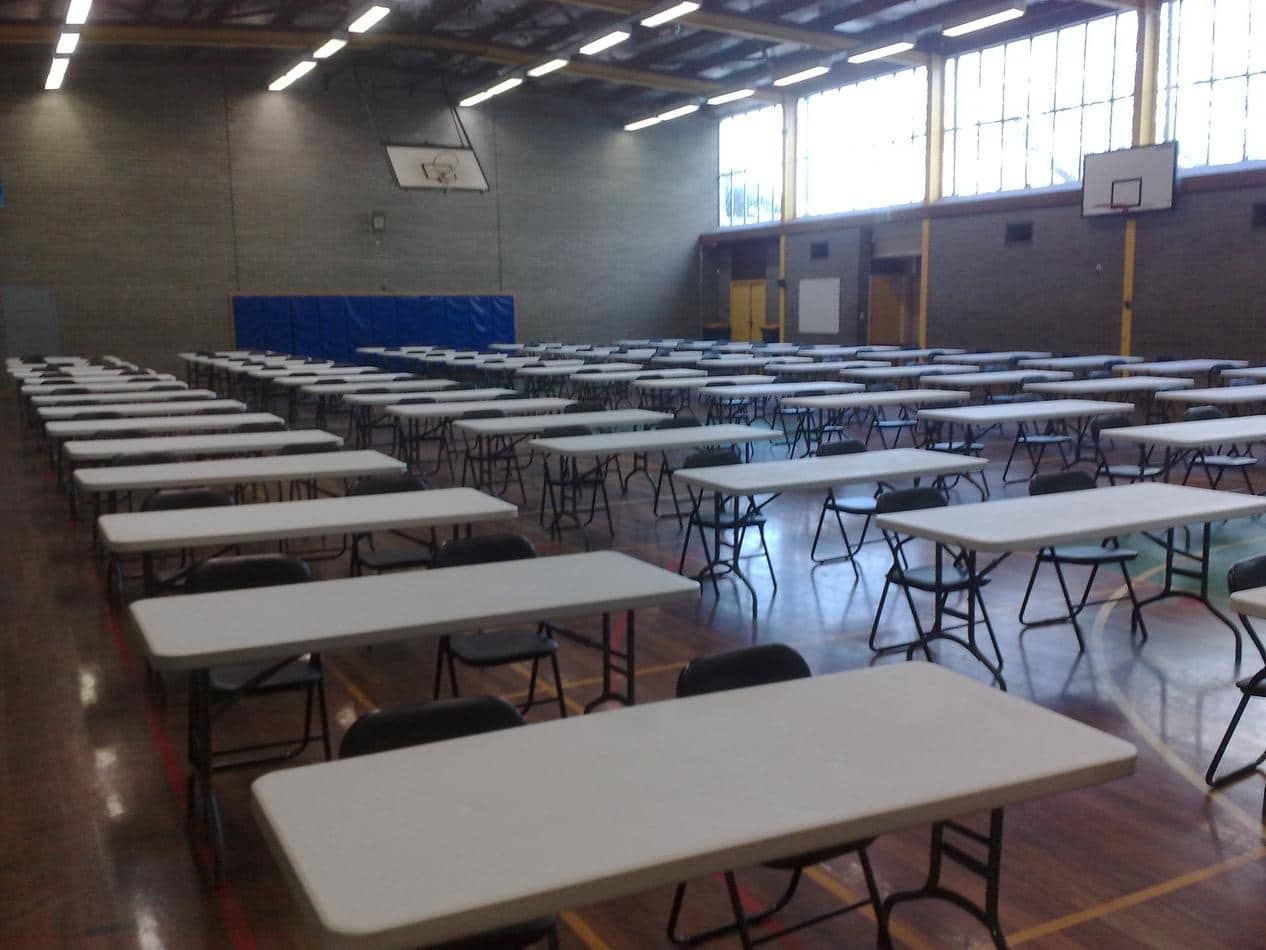 A large gymnasium filled with plastic tables and chairs.