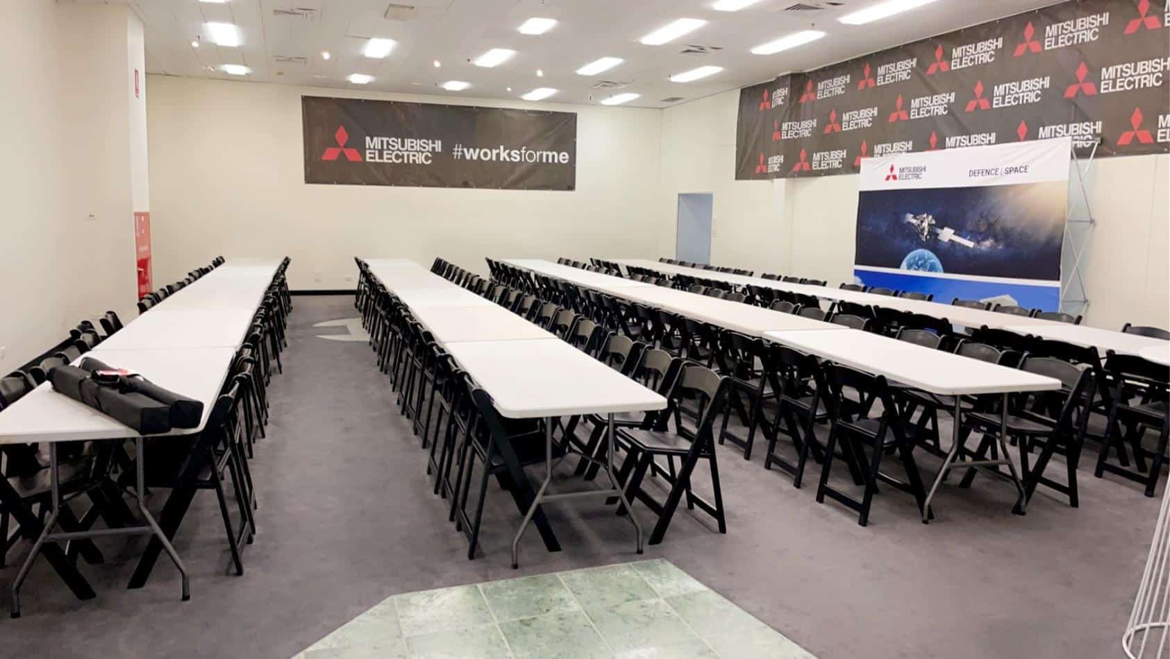 A room with plastic trestle tables and chairs set up for a meeting.