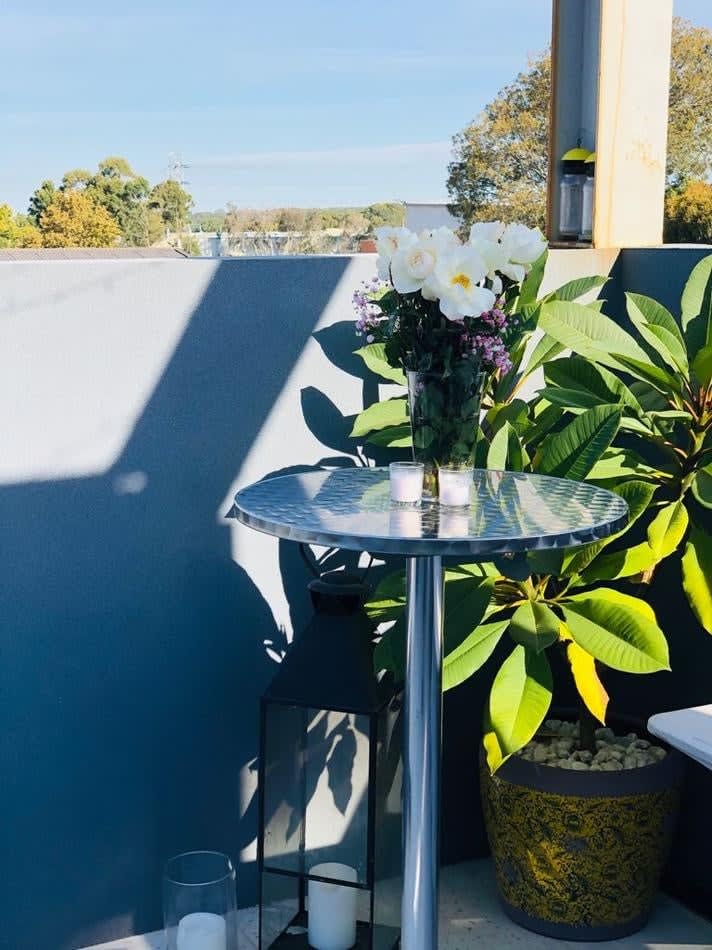 A stainless steel table and chairs on a balcony with potted plants.