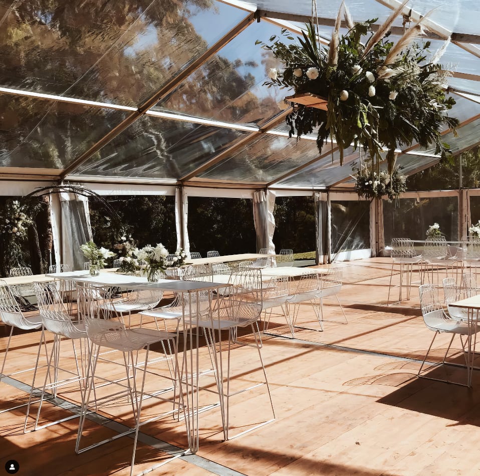 A white tent with tables and chairs in it, featuring a White High Bar Table with a White Top.