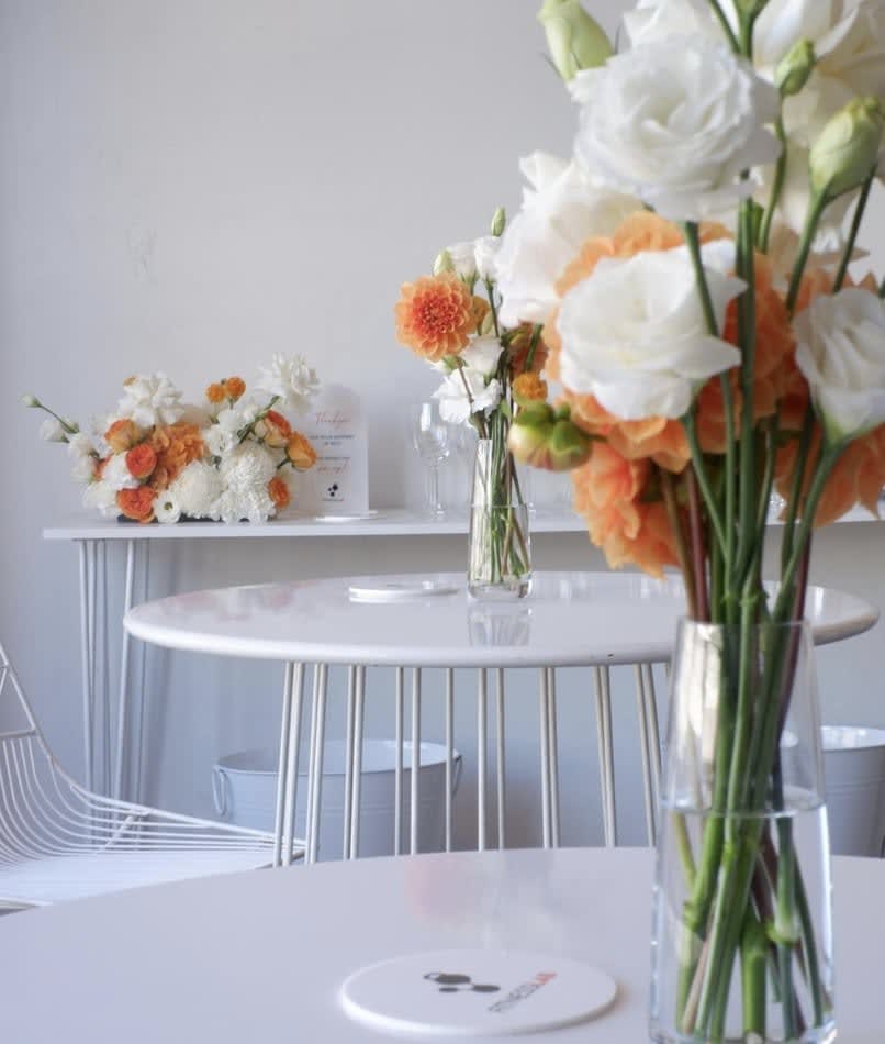 A white table with orange and white flowers on it available for White Wire Cocktail Table Hire.