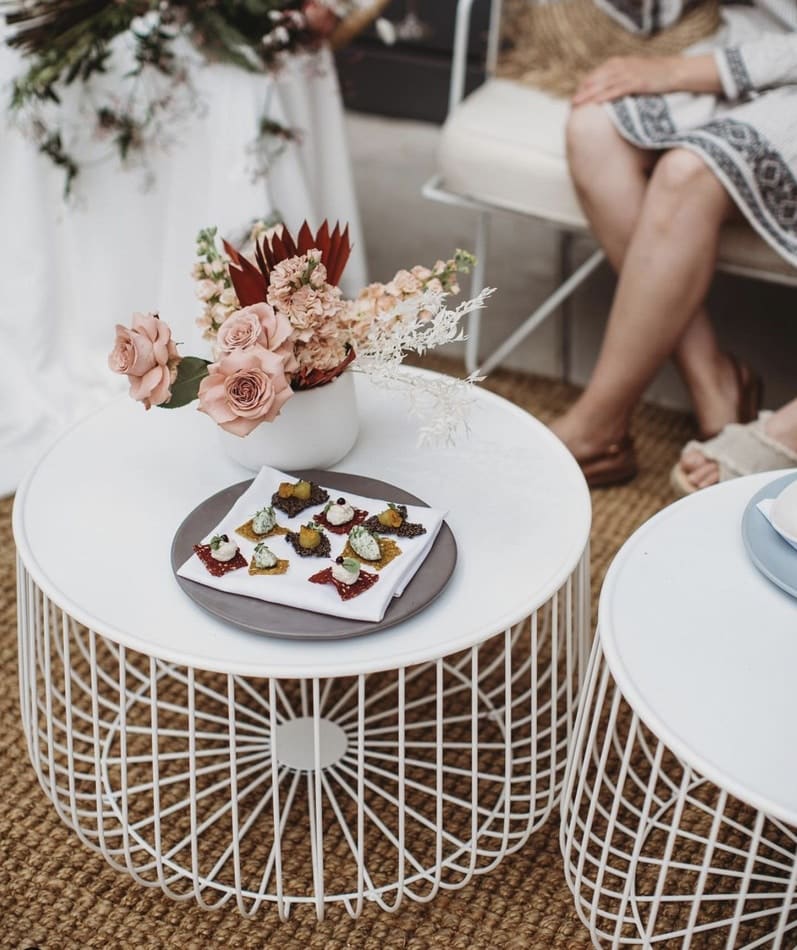 A white wire coffee table adorned with flowers, available for hire.